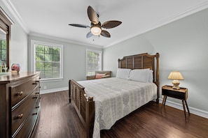 A bedroom with a wooden bed, a ceiling fan, a dresser, and a nightstand with a lamp.