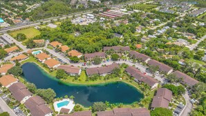 Vista aérea de una zona residencial con un lago central, rodeada de casas y un edificio grande con estacionamiento.