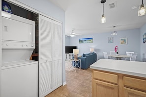 Cozinha compacta com geladeira embutida, sala de jantar com mesa e cadeiras, e sala de estar com sofá e televisão.