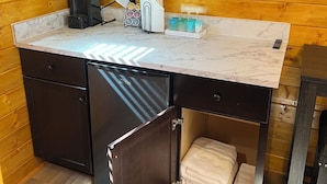 Une cuisine compacte dotée d’un plan de travail en marbre, d’une machine à café, d’un distributeur d’essuie-tout et d’un petit réfrigérateur.