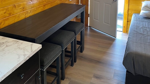 Un intérieur en bois comprenant une table à manger, des bancs, un lit et une porte donnant sur l’extérieur.
