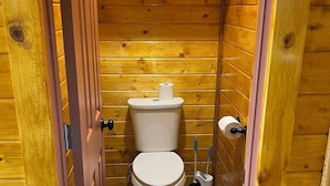 Une petite salle de bain aux murs lambrissés, équipée de toilettes, d’un porte-rouleau de papier toilette et d’une ventouse.