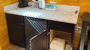 A compact kitchen with a marble countertop, a coffee machine, a paper towel dispenser, and a small refrigerator. - Sandstone Cabins at the Red Desert RV Park (Moab)