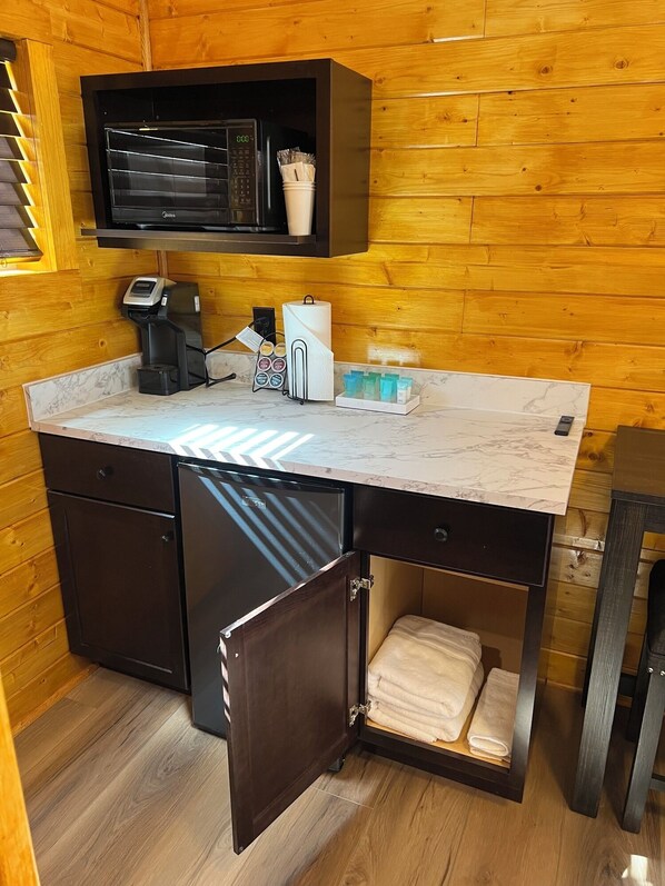 A compact kitchen with a marble countertop, a coffee machine, a paper towel dispenser, and a small refrigerator.