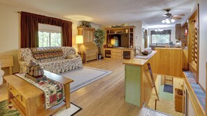 A spacious living room with a sofa, coffee table, and a fireplace. There is a kitchen area with wooden cabinets and a dining table. - Peaceful Carrollton Retreat w/ Deck & Fire Pit! (Carrollton)