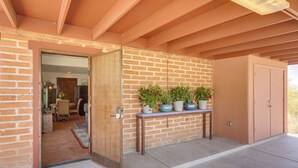 Un espacio al aire libre cubierto con un muro de ladrillo, una puerta de madera y un banco con plantas en macetas.
