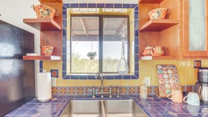 Una cocina con un lavamanos doble, estantes de madera con macetas decorativas, una ventana con vistas y un salpicadero de azulejos.