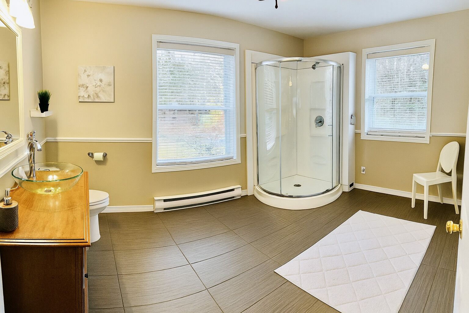 Une salle de bain avec une douche à parois de verre, un meuble-lavabo en bois, des toilettes et une chaise blanche.