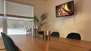 A dining area with a wooden table, four chairs, and candles on small stands. A fireplace is visible on the wall.
