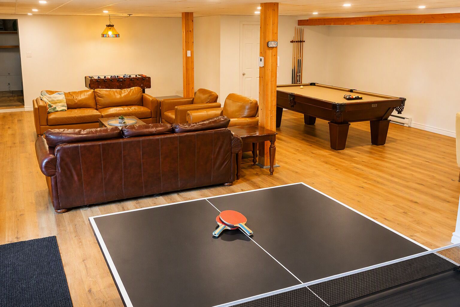 A room with a pool table, a foosball table, and a leather couch.
