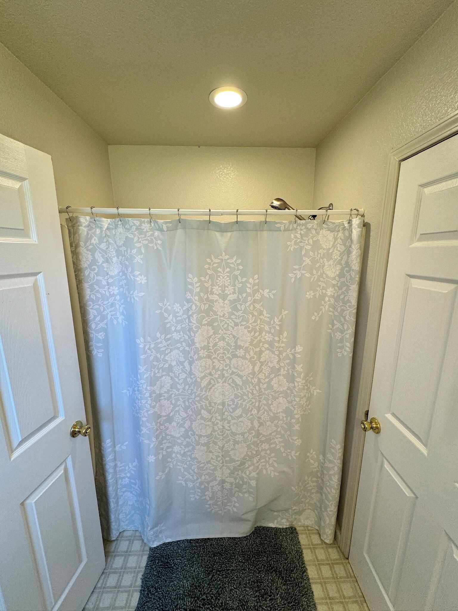 A bathroom with a shower curtain, a small rug, and two doors.