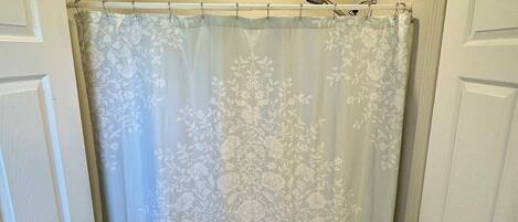 A bathroom with a shower curtain, a small rug, and two doors.