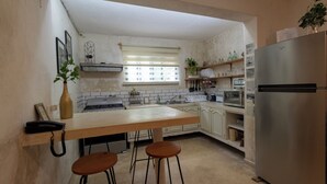 A kitchen with a wooden countertop, two stools, a refrigerator, and a window with blinds.