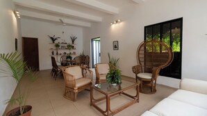 A spacious living room with a dining area, wicker furniture, and potted plants.