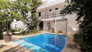 A swimming pool surrounded by potted plants and a staircase leading to a balcony.