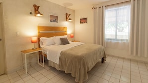 A bedroom with a wooden headboard, two bedside tables with lamps, a bed with a beige blanket, and a window with curtains.