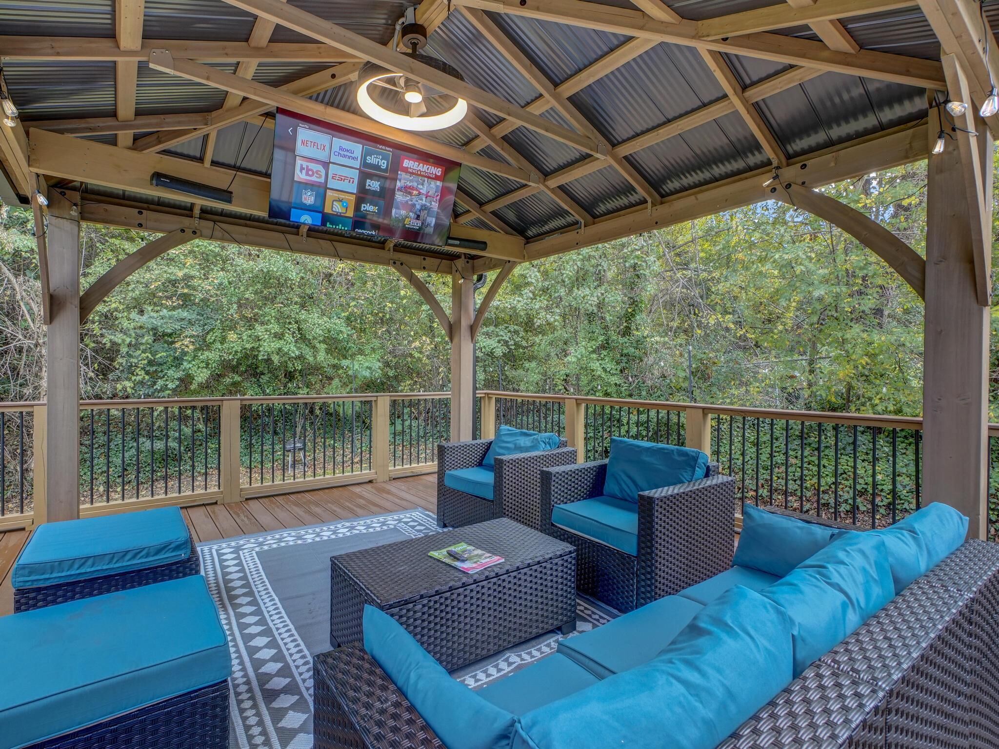 A covered outdoor deck with wicker furniture and a flat-screen TV displaying various channels.