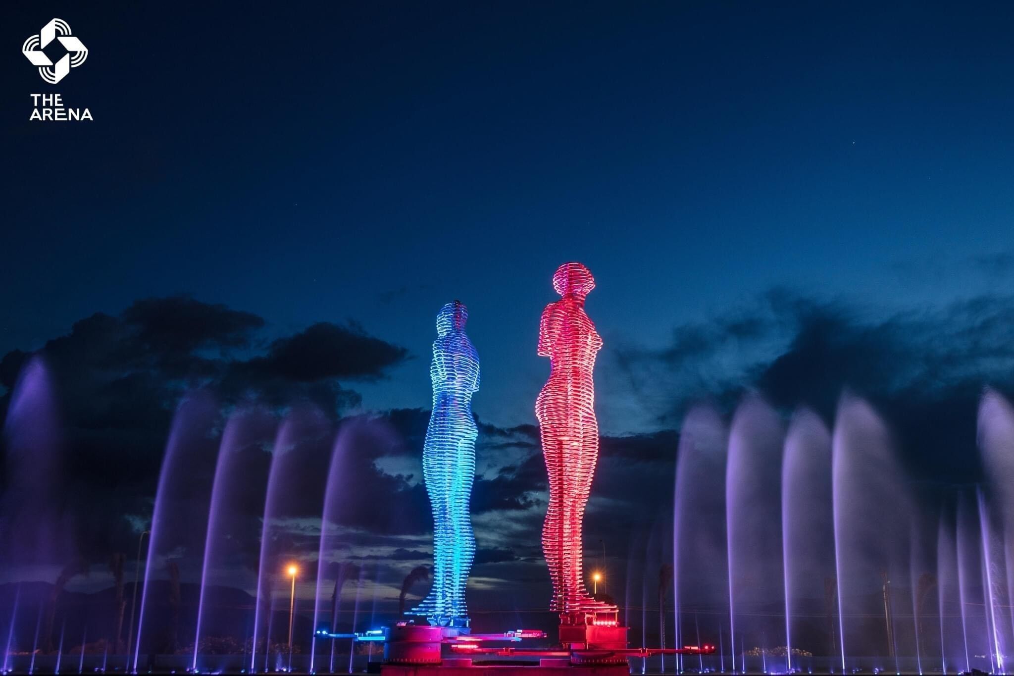 A nighttime view of a fountain display with illuminated figures and water jets.