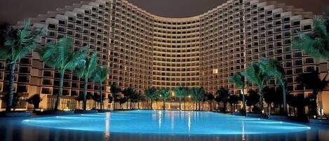A large, modern hotel with a curved facade and a central swimming pool.