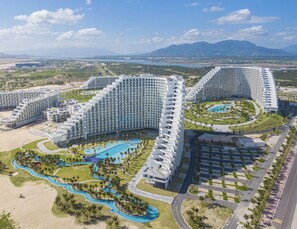 A large resort with multiple high-rise buildings, a central swimming pool, and a beach area.