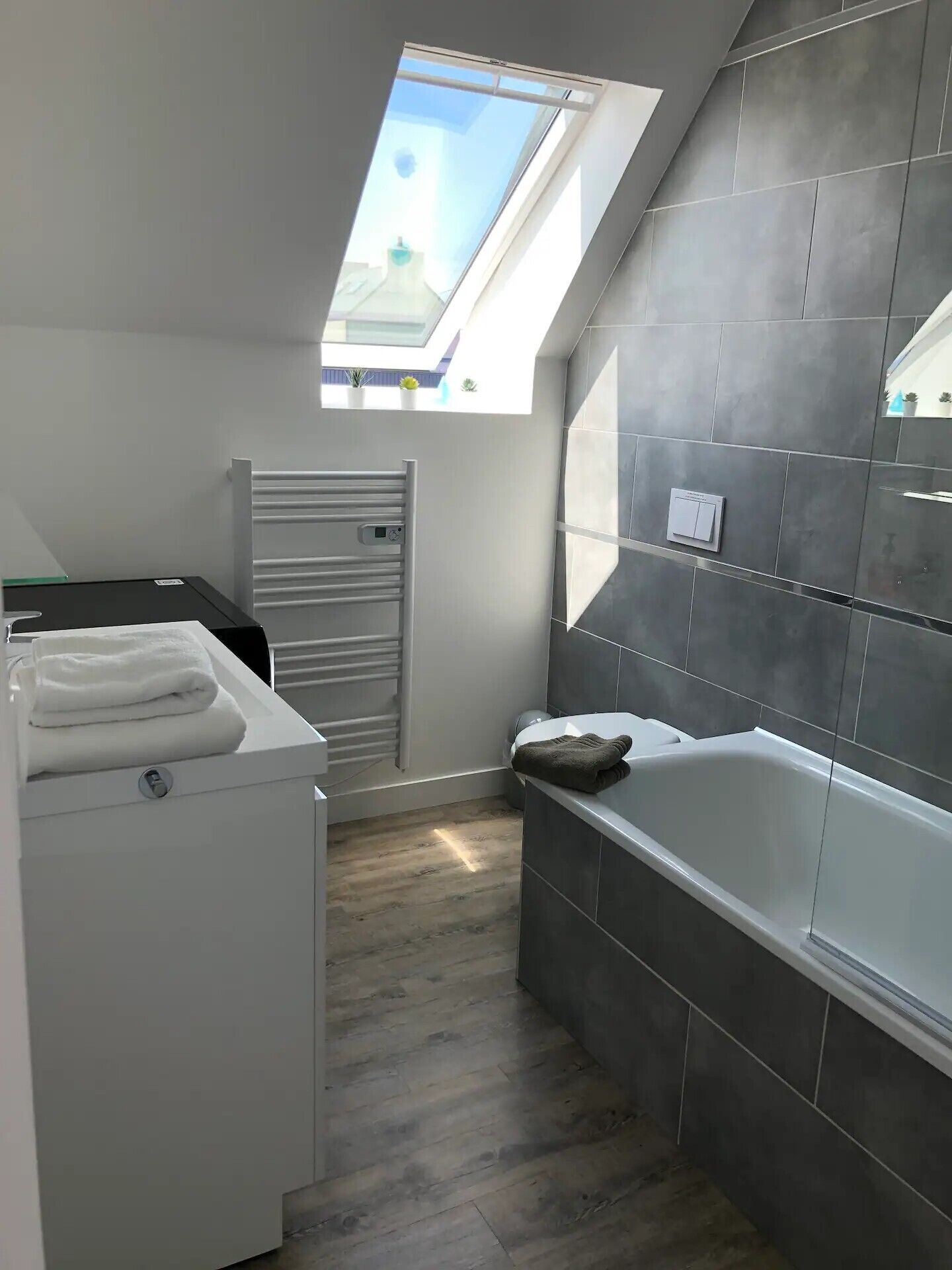 Een moderne badkamer met dakraam, ligbad en een witte wasmachine.