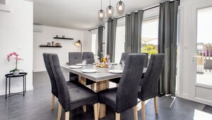 A modern dining area with a rectangular table, six grey upholstered chairs, and a chandelier. - Maison avec piscine - accès plage à pied (Plouescat)