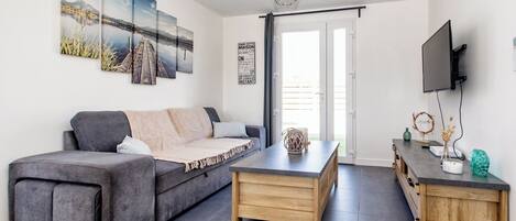 Una sala de estar moderna con un sofá gris, una mesa de centro de madera y un televisor sobre un mueble de madera.