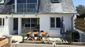A modern two-story house with a balcony, a dining area with outdoor seating, and a barbecue grill. - Maison avec piscine - accès plage à pied (Plouescat)