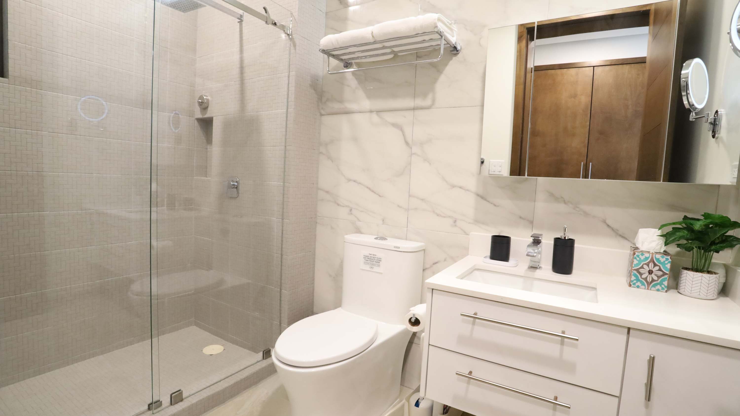 A modern bathroom with a glass shower enclosure, a toilet, a sink with a mirror, and a vanity with drawers and a cabinet.