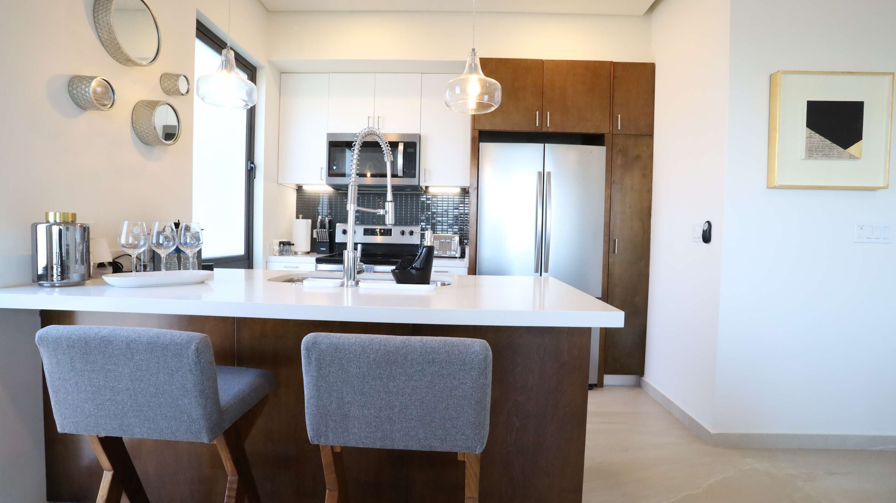 A modern kitchen with a central island, bar stools, a refrigerator, and a microwave.