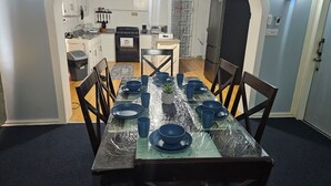 Een eetgedeelte met een tafel voor zes personen, omringd door stoelen, in een kamer met een keuken op de achtergrond.