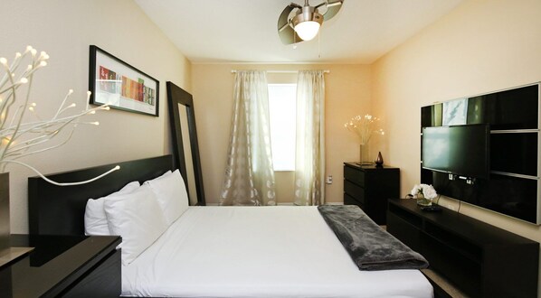 Une chambre d’hôtel avec un grand lit, un téléviseur à écran plat, une table de chevet, une commode et une fenêtre avec des rideaux légers.