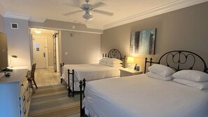 Een hotelkamer met twee bedden, een bureau, een stoel, een plafondventilator en een schilderij aan de muur.