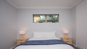 Une chambre avec un grand lit, deux tables de chevet avec des lampes, une fenêtre donnant sur un paysage verdoyant et un plaid bleu.
