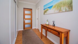 Un couloir avec une porte en bois, un tableau représentant une plage et un bureau en bois sur lequel se trouvent une bouteille et des bâtonnets d’encens.