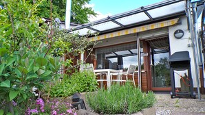 A house with a patio area featuring a table and chairs, a concrete planter with plants, and a garage door. - Grill, Überdachte Terrasse, Sonnenschirm, 2 Einzelbetten, 2xtv, Küche, Ww-knoten (Greifenstein)