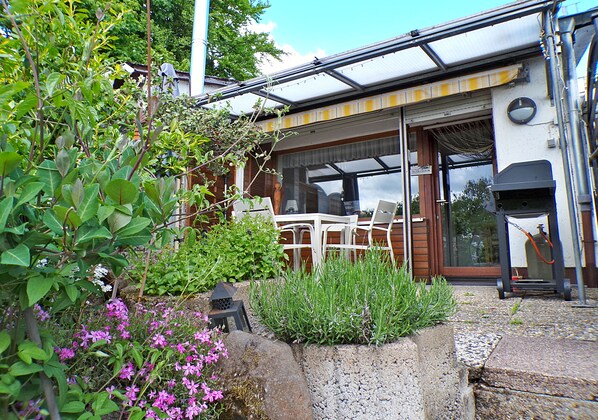 A house with a patio area featuring a table and chairs, a concrete planter with plants, and a garage door.