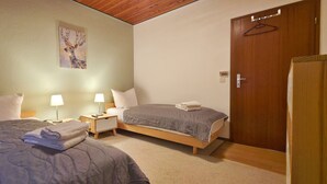 A hotel room with two beds, a painting on the wall, a wooden door, and a nightstand with lamps. - Grill, Überdachte Terrasse, Sonnenschirm, 2 Einzelbetten, 2xtv, Küche, Ww-knoten (Greifenstein)