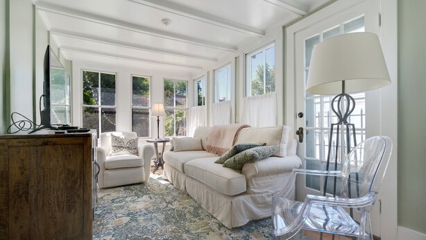Un salon spacieux avec une grande fenêtre, un canapé blanc, un meuble en bois et une chaise transparente.
