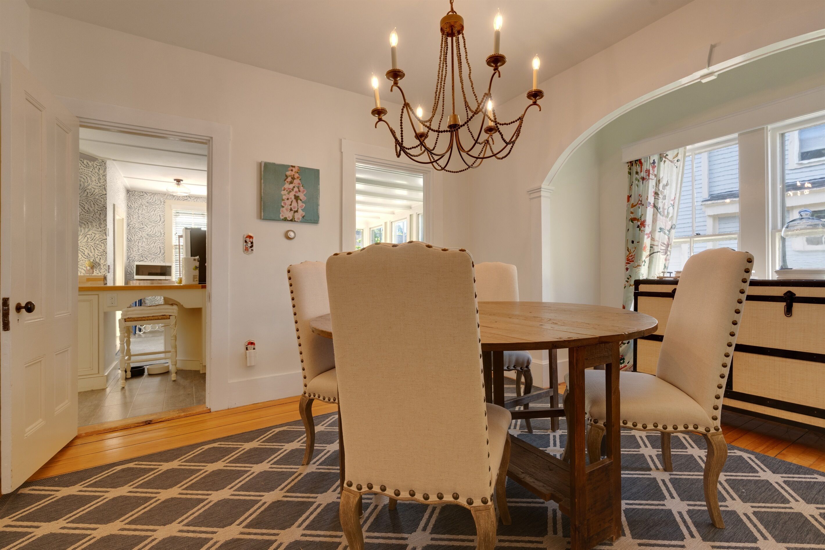 A dining area with a round wooden table and four upholstered chairs with decorative studs. A chandelier hangs above the table.