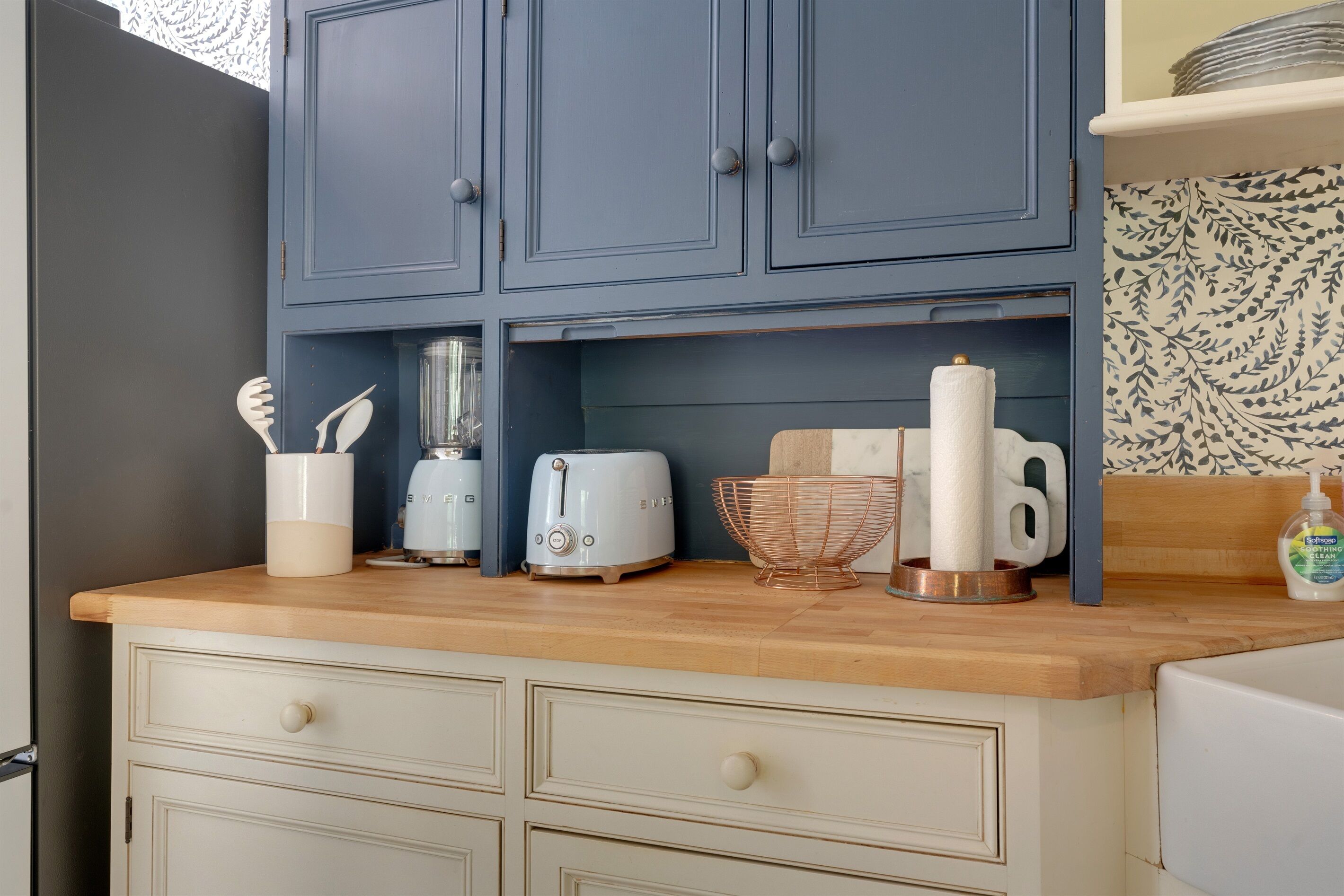 Una cucina con piano di lavoro in legno, un pensile blu, un tostapane, una macchina da caffè e un lavello.