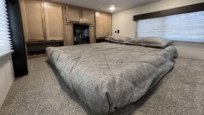 A bedroom with a large bed, wooden cabinets, and a window with blinds. - Ridgetop Retreat Tiny Home, Dakota MN (Dakota)