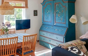A room with a dining table, chairs, a TV, a blue cabinet, and a lamp.