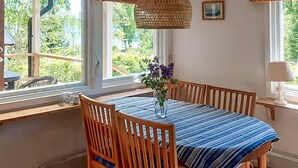 Zona pranzo con tavolo apparecchiato per due, sedie in legno, un vaso con fiori e vista sul verde circostante.