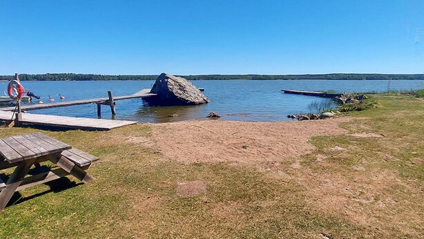 Un'area pic-nic sul lago con un molo di legno, una formazione rocciosa e un galleggiante di salvataggio.