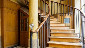 A grand staircase with a wooden finish and black balusters, leading to a landing with a large wooden door.