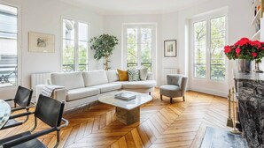 A modern living room with a herringbone wooden floor, a white sofa, a grey armchair, and a coffee table.