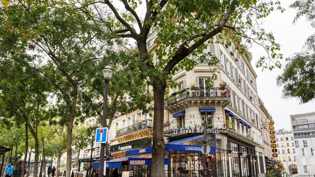 A multi-story building with a restaurant on the ground floor, a blue awning, and a sign reading "Le Bonheur de Vivre".