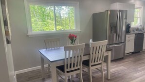 Une cuisine moderne avec une table à manger, des chaises, un réfrigérateur et une fenêtre donnant sur des arbres.