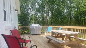 Une terrasse en bois avec une table de pique-nique et des chaises rouges, un barbecue et un bâtiment blanc en arrière-plan.